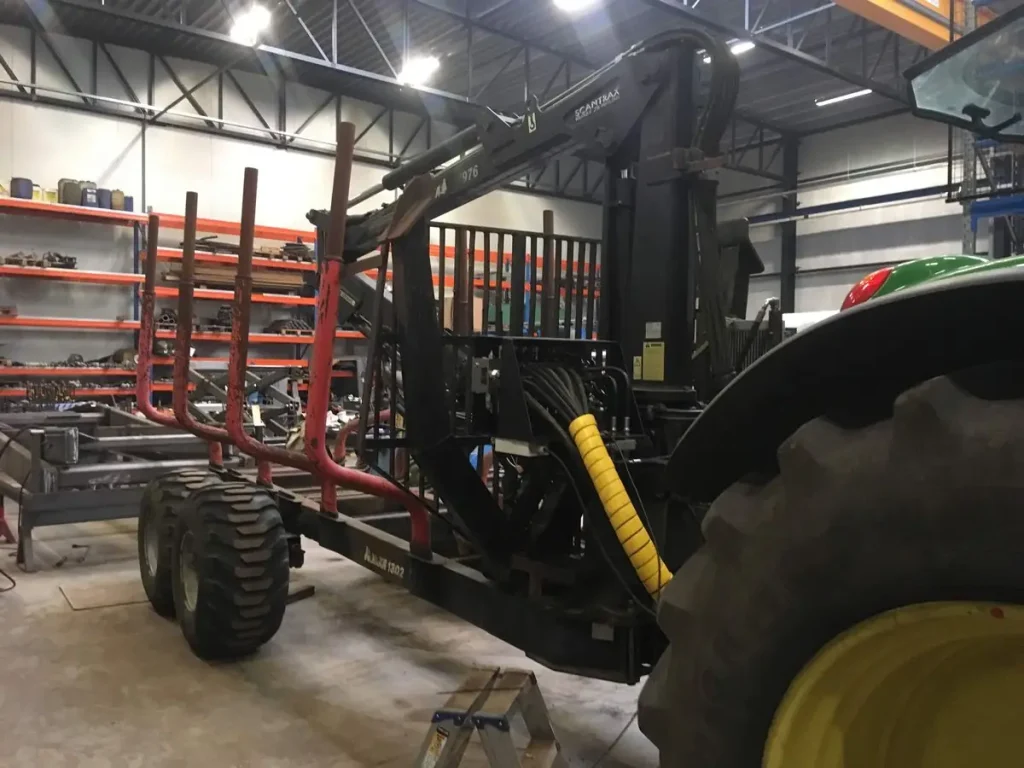 Tractor met hydraulische boomkraan op een houtaanhangwagen in de werkplaats
