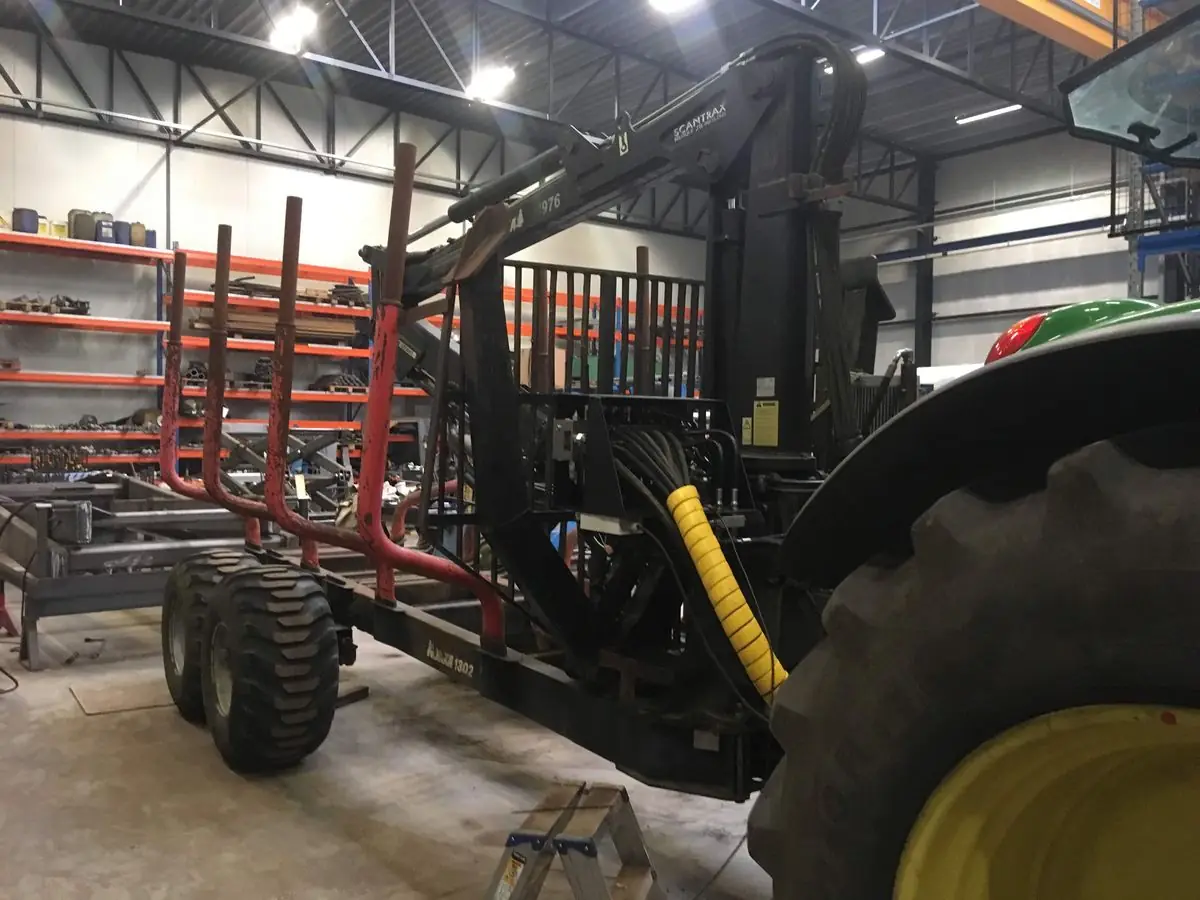 Tractor met hydraulische boomkraan op een houtaanhangwagen in de werkplaats